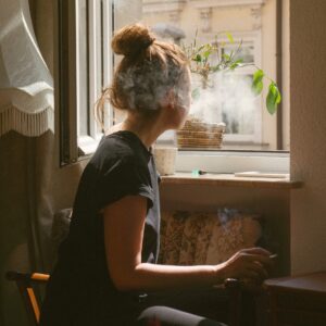 a woman who might have Cannabis Use Disorder sits in a window smoking