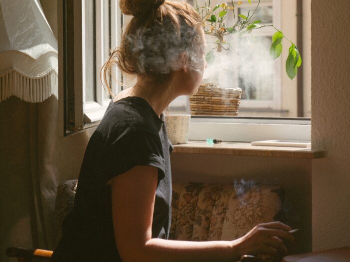 a woman who might have Cannabis Use Disorder sits in a window smoking